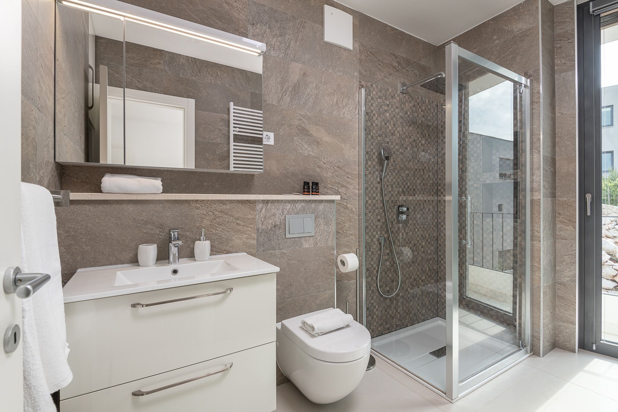 A modern bathroom with a glass-enclosed shower, a white sink, and a toilet.