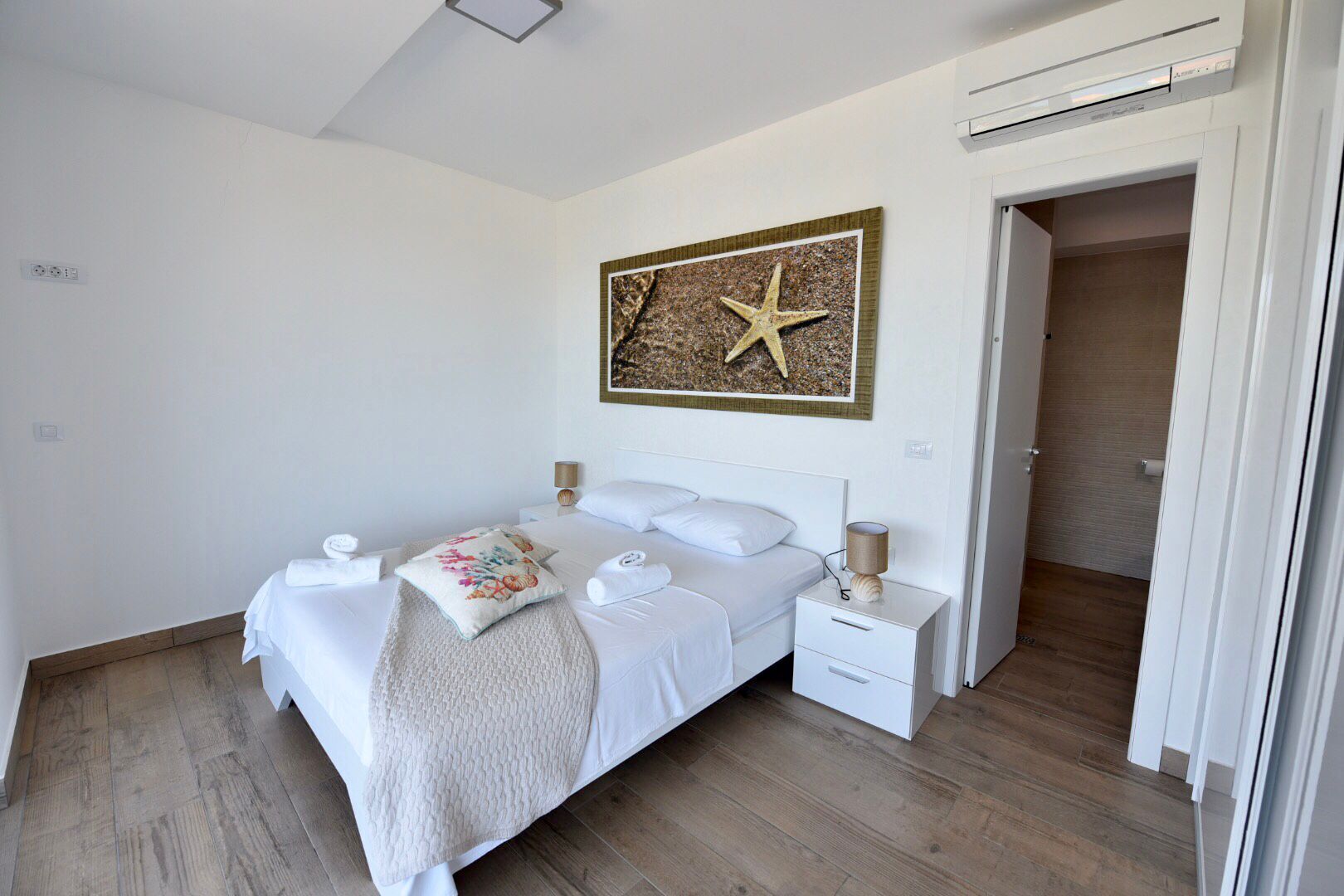 A bedroom with a bed, bedside tables, a starfish artwork, and a door leading to a bathroom.