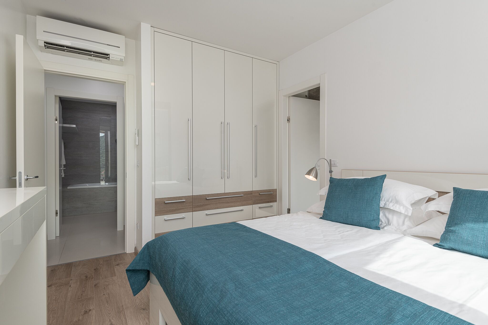 A bedroom with a bed, white wardrobe, and a bathroom visible through an open door.