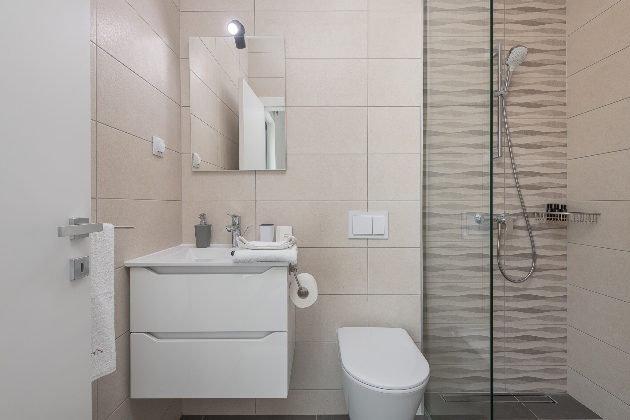 Een moderne badkamer met een douchecabine van glas, een witte wastafel en een toilet.