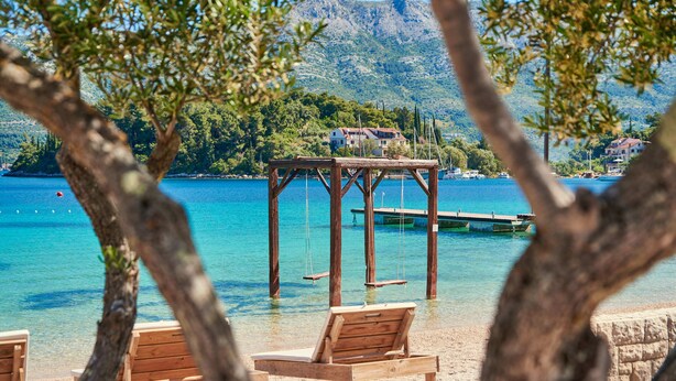 Una terraza de madera con columpios sobre un lago azul cristalino, rodeada de árboles y una montaña distante.