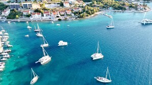 Un pueblo costero con numerosos veleros amarrados en un puerto deportivo, rodeado de edificios residenciales y exuberante vegetación.