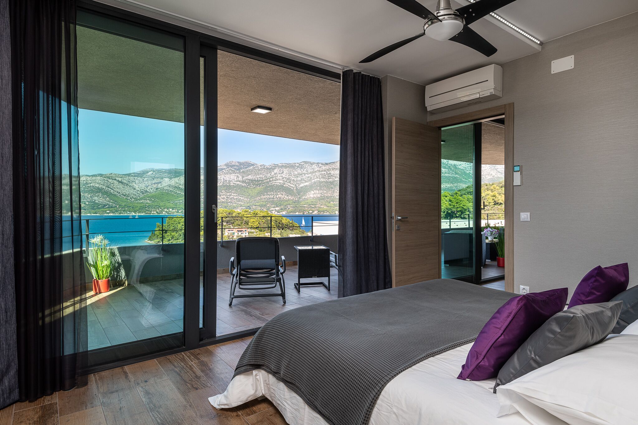 A bedroom with a large bed, a ceiling fan, and a view of a balcony with a chair and table.