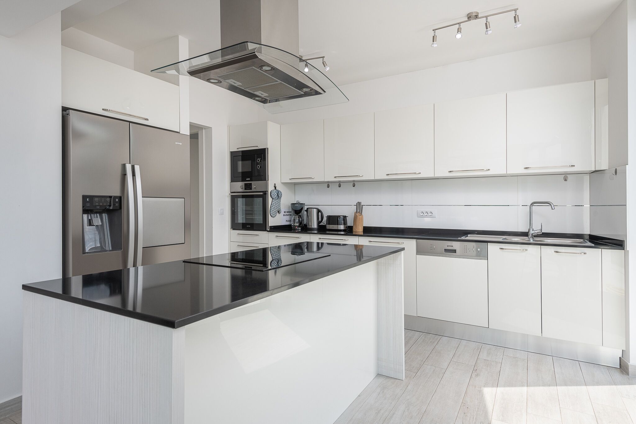 A modern kitchen with white cabinetry, a stainless steel refrigerator, a built-in oven, and a black countertop island.