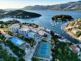 Un pueblo costero con edificios modernos, una cancha de tenis y un puerto deportivo con barcos.