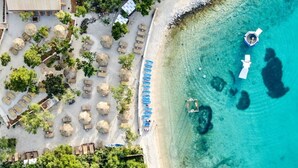 Vista aérea de un complejo turístico frente a la playa, con tumbonas, sombrillas y una zona para nadar.