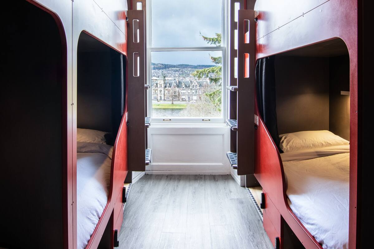 Un compartiment de train avec deux lits, une fenêtre donnant sur une ville et un plancher en bois.