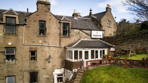 A historic stone building with a sign for 'Bazpackers' and a small garden area with a wooden fence and a bicycle. - Bazpackers Hostel (Inverness)