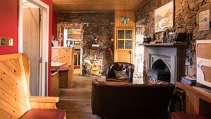 A cozy room with a fireplace, wooden furniture, and a stone wall. - Bazpackers Hostel (Inverness)