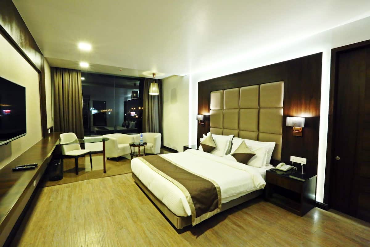 Habitación de hotel moderna con una cama grande, un escritorio, una silla, un televisor y vistas a la ciudad de noche.