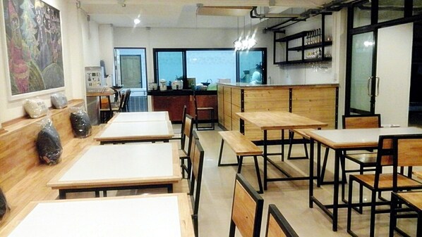 A restaurant with wooden tables and chairs, a chalkboard menu, and a view of the city through large windows.