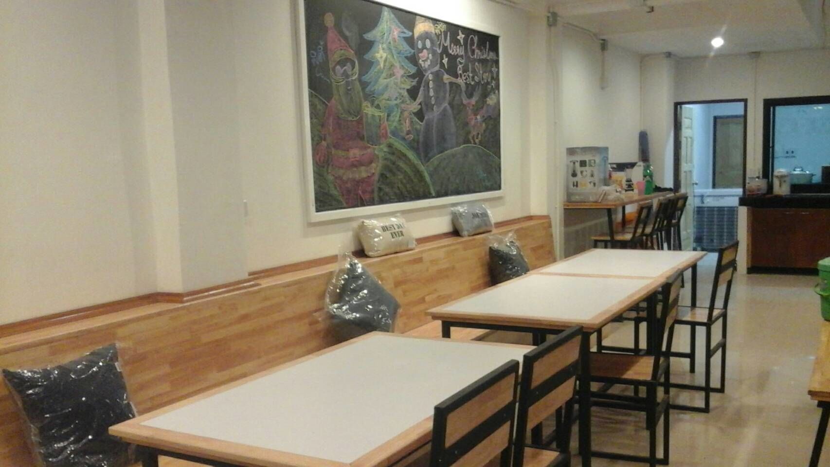 A dining area with wooden benches and tables, a large wall mural, and a kitchen in the background.