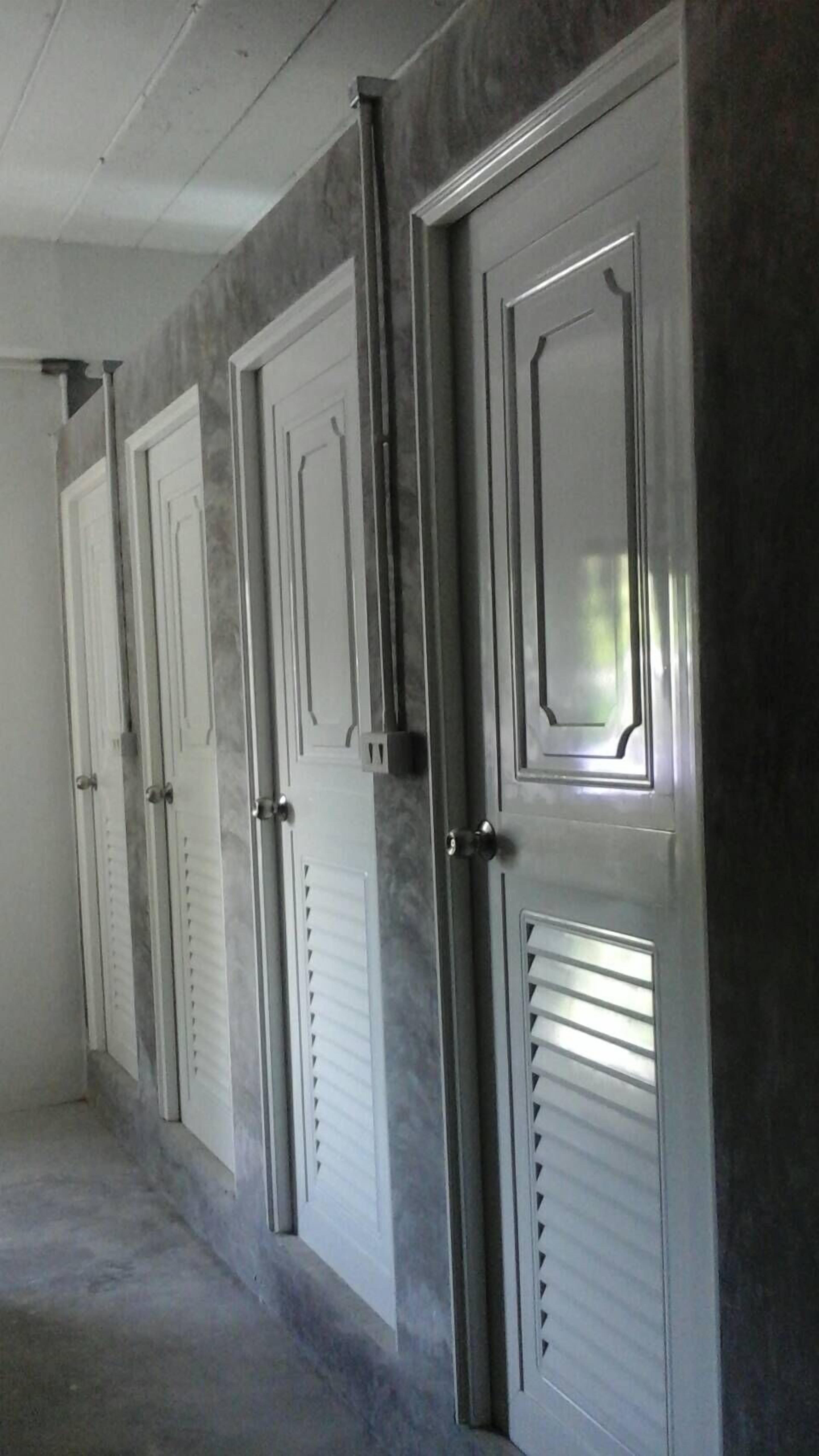 A row of closed doors with a metallic finish and a central handle, set in a hallway with a concrete floor.