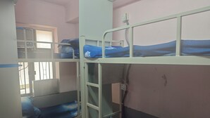 A dormitory room with bunk beds, a window with bars, and an air conditioning unit.