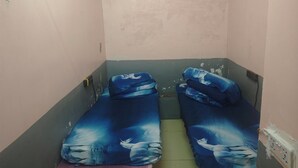 A small, narrow room with two beds featuring a blue and white design, a wall-mounted air conditioner, and a power outlet.
