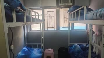 A dormitory room with bunk beds, a small stool, and a window with a view.