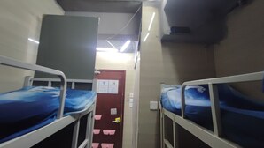 A narrow corridor with bunk beds on either side, a door with a lock, and a light fixture above.