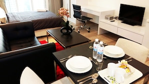 A hotel room with a bed, a desk, a TV, a dining table set with plates, cutlery, and water bottles.