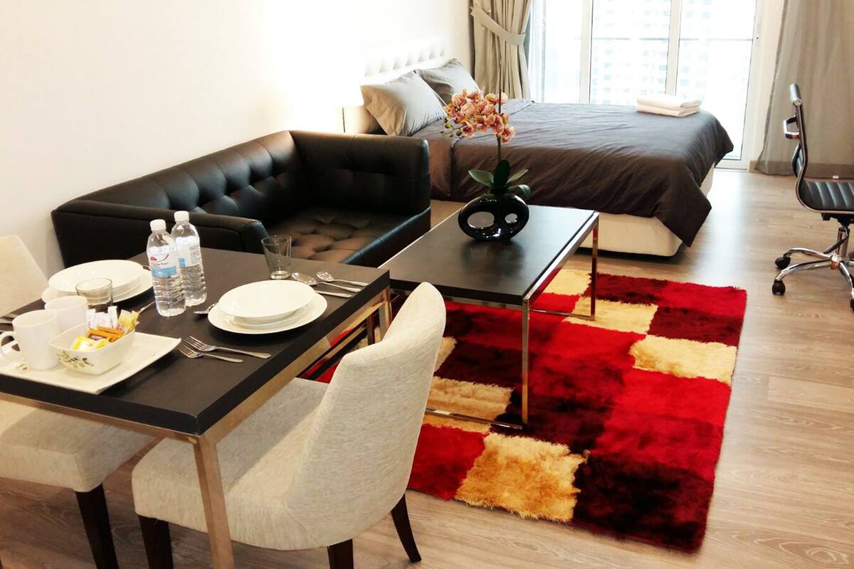 A modern hotel room with a dining area, a sofa, a bed, and a desk.