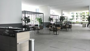 A spacious indoor area with multiple seating arrangements, including tables and chairs, and several potted plants.