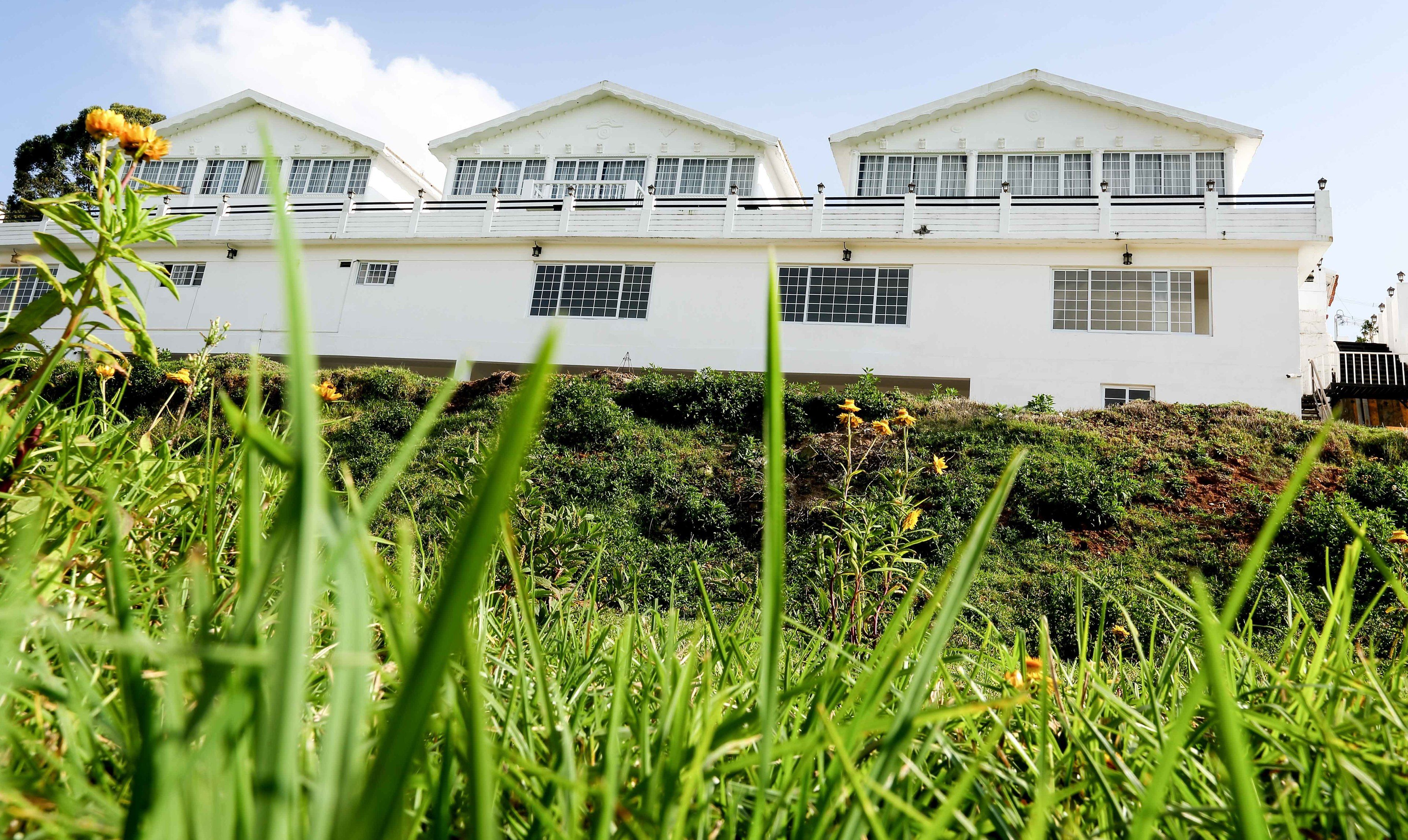 Een wit gebouw met veel ramen en balkons, omgeven door groen gras en planten.