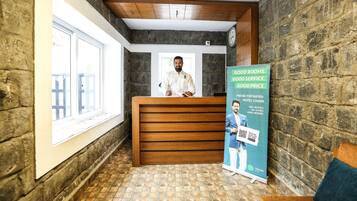 Een hotel receptie met een houten balie, een receptionist en een promotieposter.