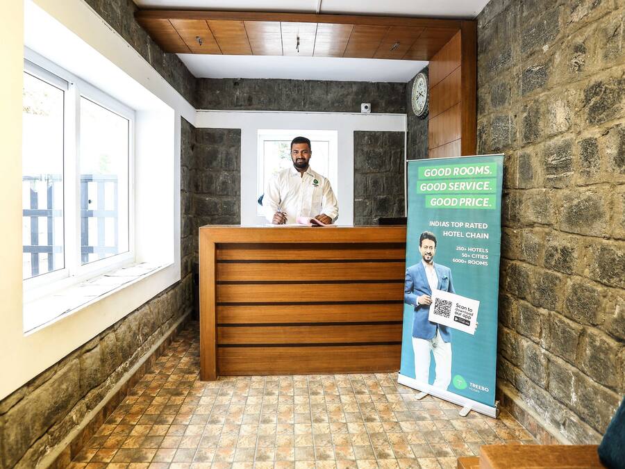 Een hotel receptie met een houten balie, een receptionist en een promotieposter.