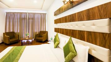 A hotel room with a large bed, two armchairs, a wooden headboard, and a chandelier.