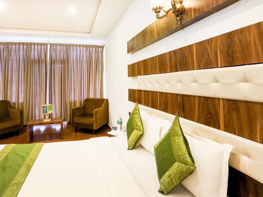 A hotel room with a large bed, two armchairs, a wooden headboard, and a chandelier.