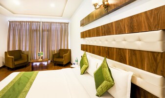 A hotel room with a large bed, two armchairs, a wooden headboard, and a chandelier.