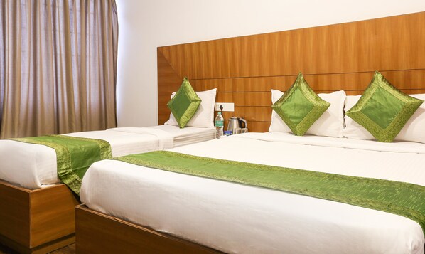 A hotel room with two beds, a wooden headboard, and green decorative pillows.