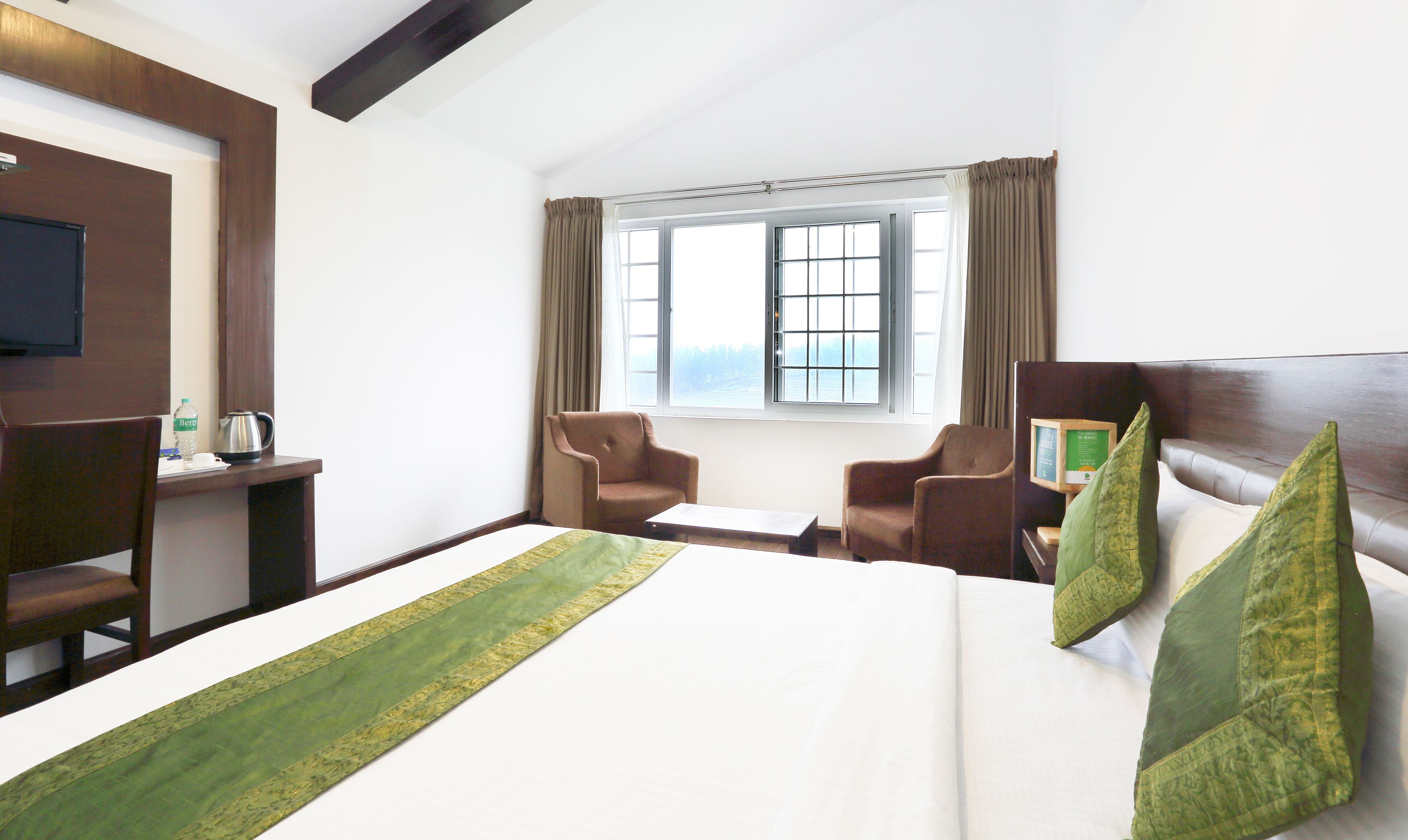 A hotel room with a bed, two armchairs, a desk, a television, and a window with curtains.