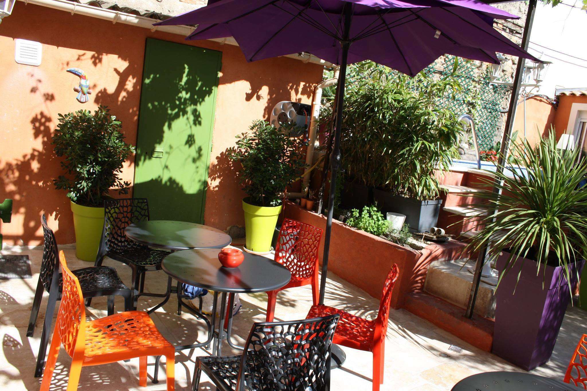 An outdoor patio with a table and chairs, surrounded by potted plants and a green door.