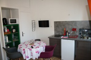 Een functionele keuken met een magnetron, een kleine koelkast, een spoelbak en een eethoek met een tafel en stoelen.