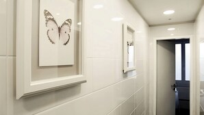 A hallway with white tiled walls, a framed butterfly artwork, and a mirror. - Sleephotels (Hamburg)
