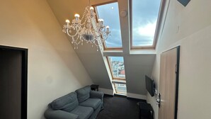 A room with a sloped ceiling, a grey sofa, a chandelier, and skylights. - Sleephotels (Hamburg)