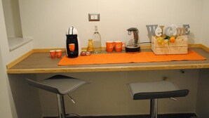 A small bar area with a coffee machine, mugs, a bottle, and a welcome sign. - Bien-Bì (Naples)