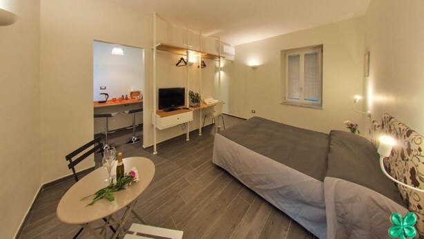 A compact living space with a bed, a dining table with chairs, a kitchenette, and a TV. - Bien-Bì (Naples)