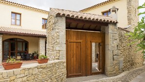 A stone-walled entrance with a wooden door, a patio with outdoor seating, and a building with a tiled roof. - Albergo Diffuso Il Mandorlo (Baressa)