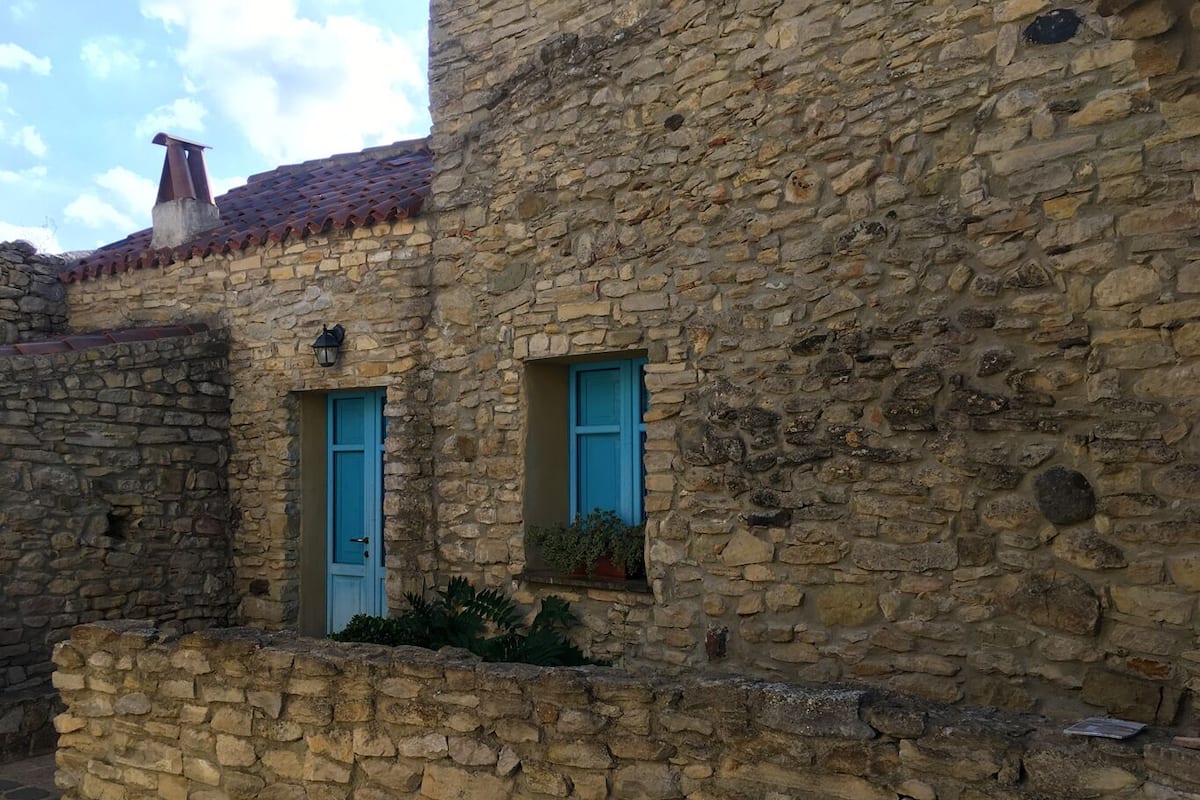 A stone building with two blue doors and a small window with a plant.
