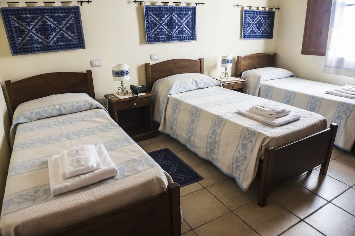 A hotel room with two single beds, a nightstand with a lamp, and a small table with a phone.