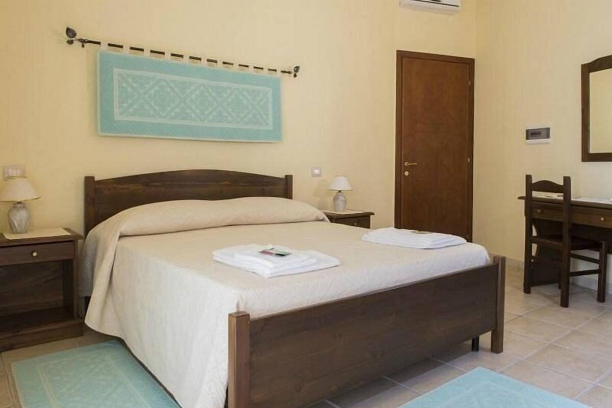 A bedroom with a wooden bed, two bedside tables with lamps, a wooden desk, and a door.