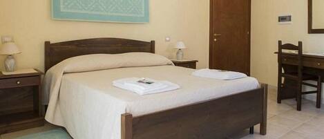 A bedroom with a wooden bed, two bedside tables with lamps, a wooden desk, and a door.