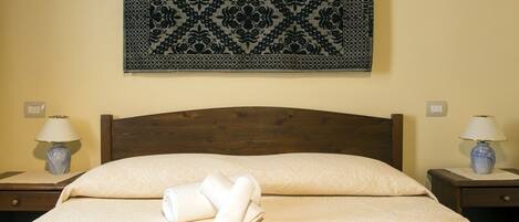 A neatly made bed with a patterned headboard, two bedside lamps, and a decorative wall hanging above.