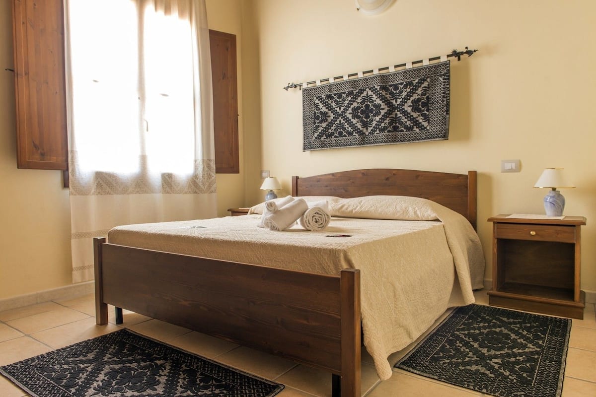 A neatly made bed with a wooden headboard, a patterned tapestry above it, and two nightstands with lamps.