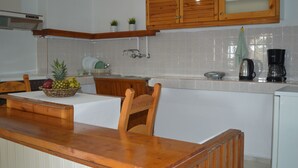 A kitchen with wooden cabinets, a white countertop, and a dining area with a table and chairs. - Sofia (Apokoronas)