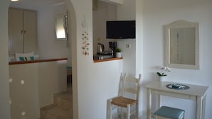 A room with a white wall, a flat-screen TV mounted above a wooden table, a white chair with a woven seat, and a small bench. - Sofia (Apokoronas)