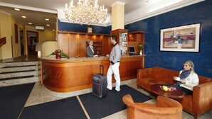 A hotel lobby with a reception desk, a chandelier, a blue wall, and a framed artwork. - Hotel Lafonte (Karlovy Vary)
