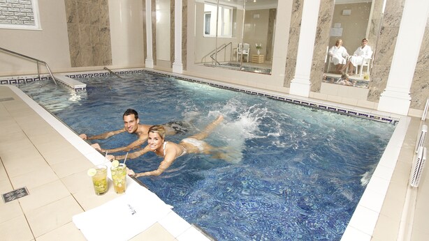 A swimming pool with a glass wall, a chair, and a table with drinks. - Hotel Lafonte (Karlovy Vary)
