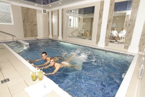 Piscina con pared de vidrio, una silla y una mesa con bebidas.